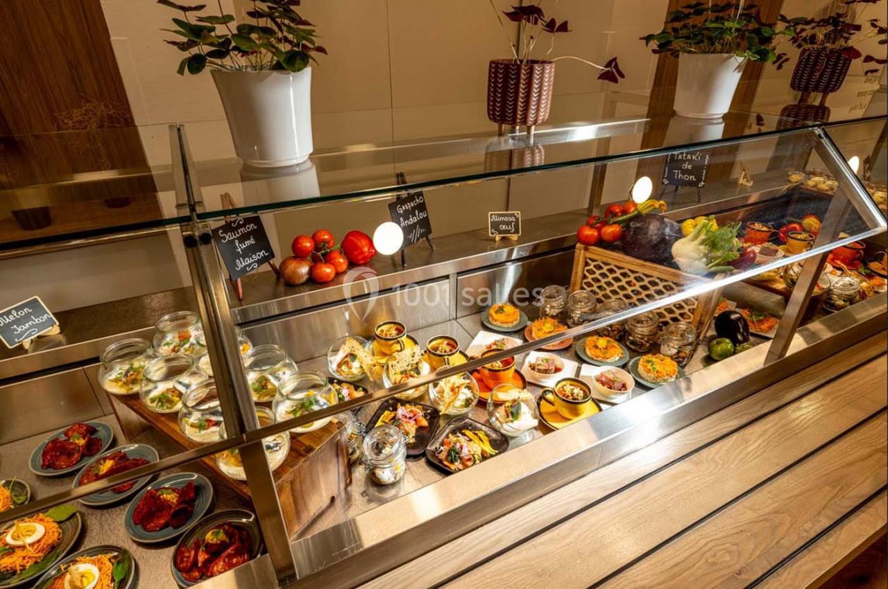 Vitrine réfrigérée présentant une variété de plats préparés, légumes frais et condiments, avec étiquettes descriptives.