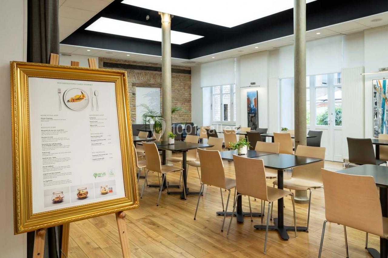 Salle de restaurant lumineuse avec des tables en bois clair, des chaises assorties et un menu encadré au premier plan.