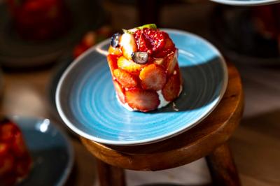Chambre lumineuse avec un lit simple, des lits superposés en bois, un bureau et une fenêtre donnant sur des toits.