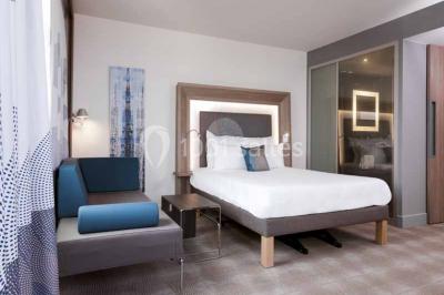 Façade d'un hôtel Novotel moderne éclairé en soirée, avec des lampadaires allumés au premier plan.