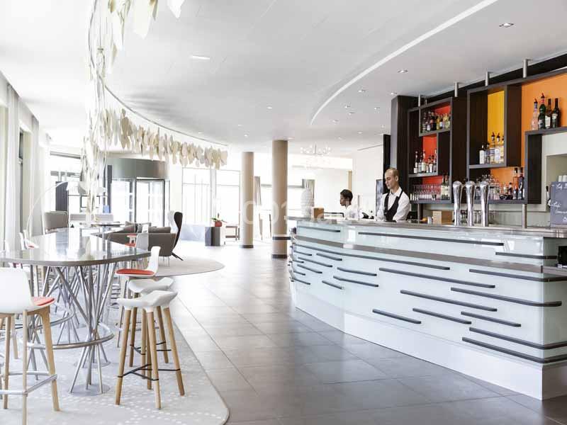Bar moderne avec comptoir lumineux, tabourets design, étagères de bouteilles et personnel en service.
