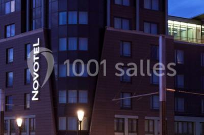 Façade d'un hôtel Novotel moderne éclairé en soirée, avec des lampadaires allumés au premier plan.