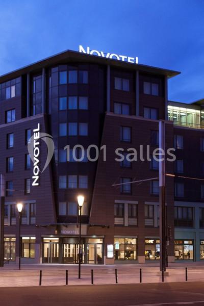 Façade d'un hôtel Novotel moderne éclairé en soirée, avec des lampadaires allumés au premier plan.