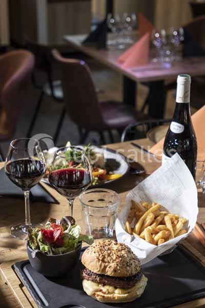 Repas composé d'un burger, frites, salade et verres de vin rouge sur une table dans un restaurant.