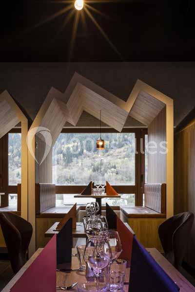 Salle de restaurant moderne avec tables dressées, baies vitrées et vue sur un paysage boisé.