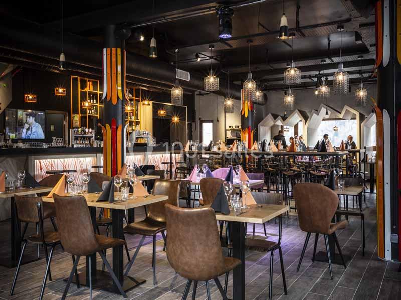 Salle de restaurant moderne avec tables en bois, chaises en cuir marron et éclairage suspendu.