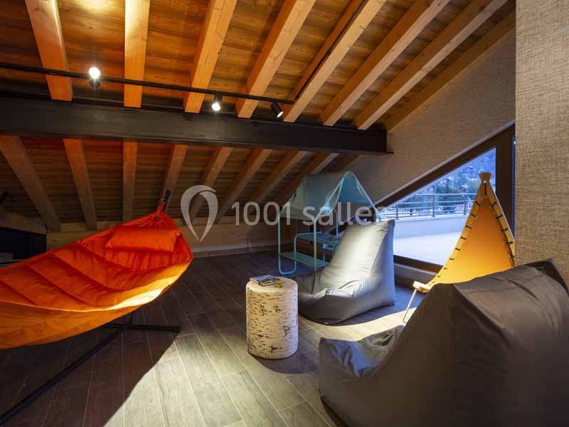 Espace sous combles aménagé avec fauteuils colorés, pouf, lumière tamisée et vue sur l'extérieur.