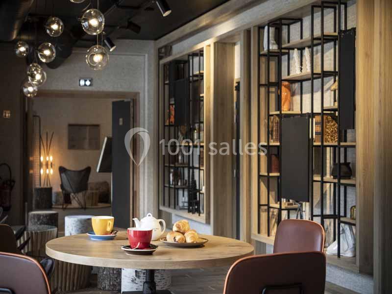 Table avec tasses, théière et viennoiseries dans un espace intérieur moderne avec étagères décoratives en arrière-plan.