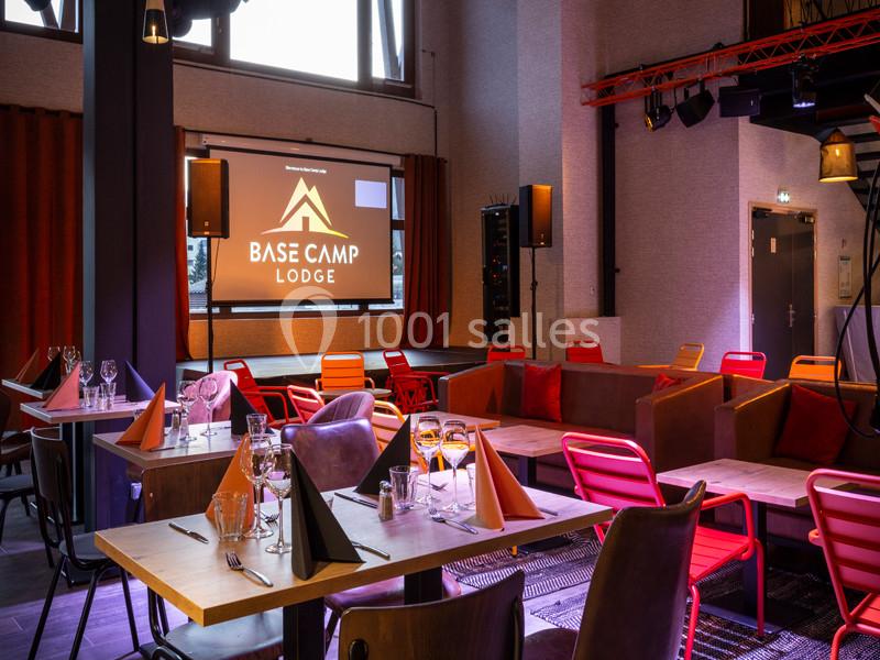 Salle de restaurant avec tables dressées, chaises colorées et écran affichant ’Base Camp Lodge’ en arrière-plan.