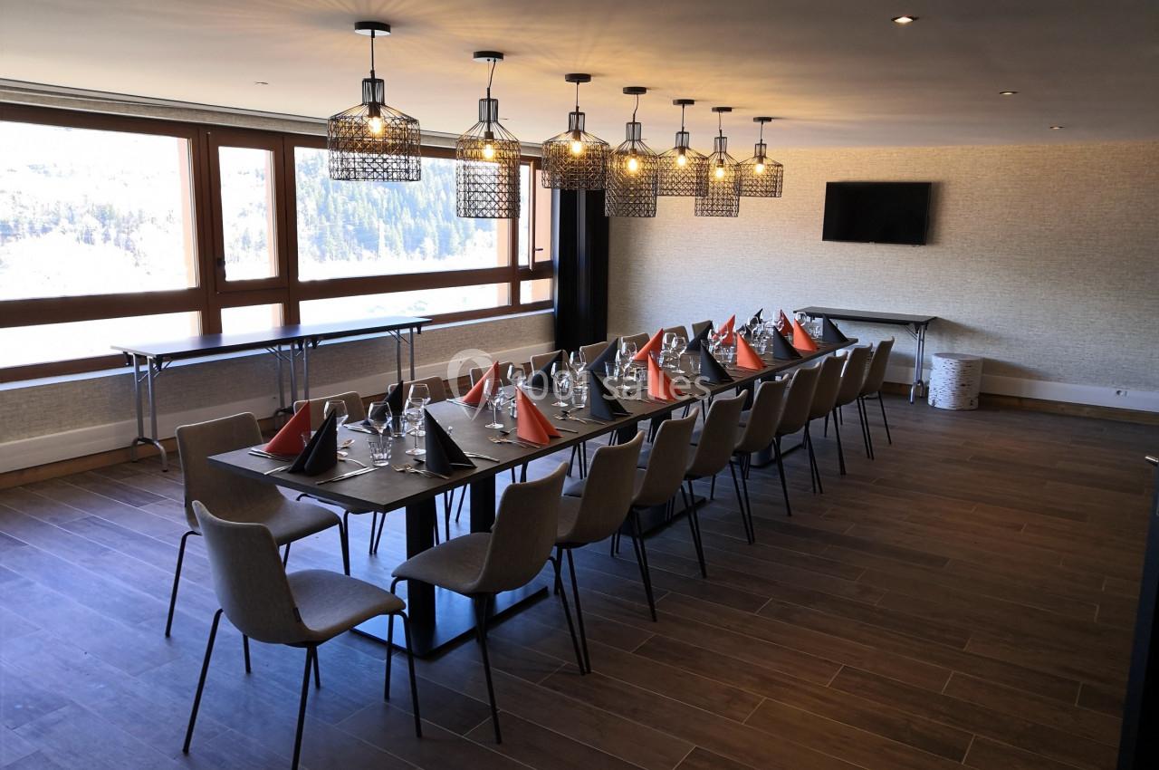 Salle de réunion lumineuse avec une grande table dressée, chaises, lustres modernes et vue sur l'extérieur.