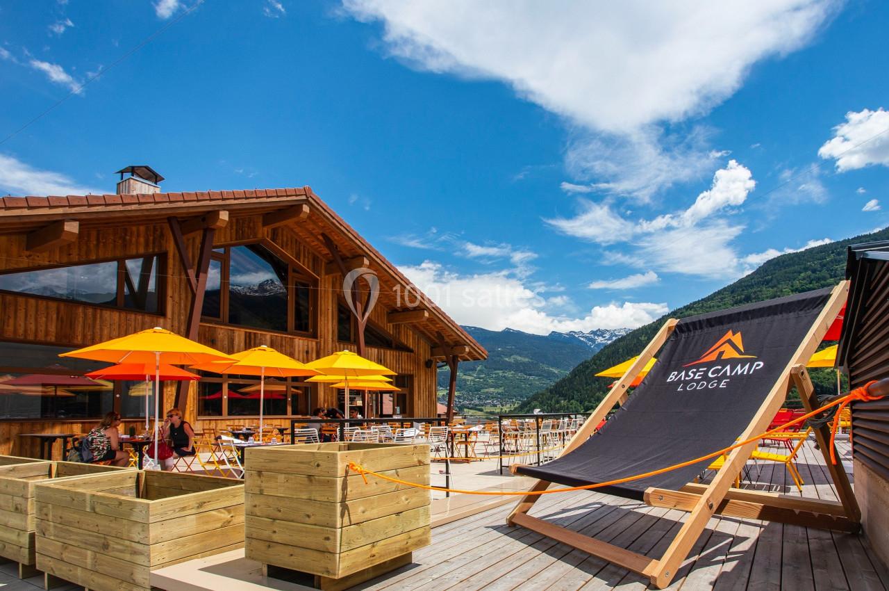 Terrasse ensoleillée avec chaises longues et parasols colorés devant un chalet en bois, vue sur les montagnes.