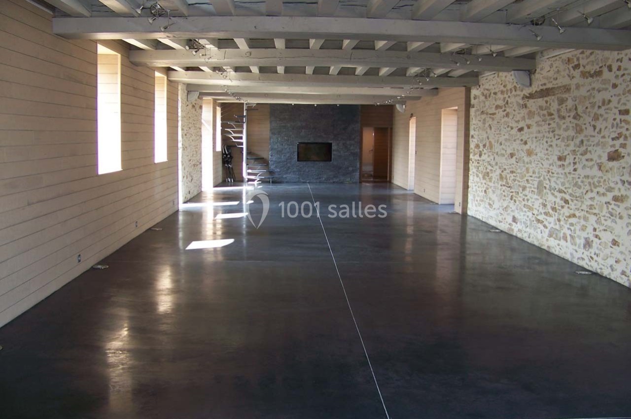 Intérieur d'une grande pièce avec sol en béton poli, murs en pierre et bois, et plafond avec poutres apparentes.