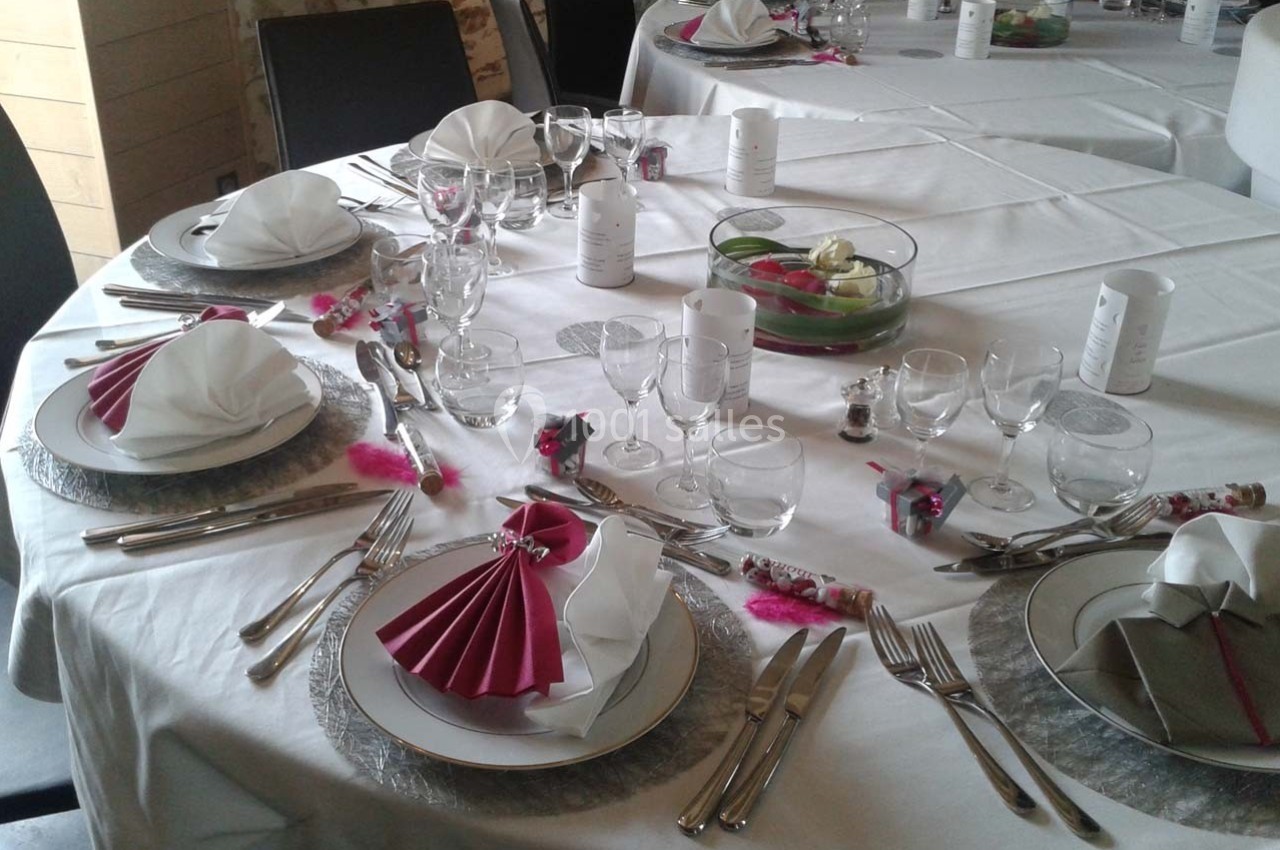 Table dressée pour un repas festif avec nappes blanches, serviettes pliées, vaisselle élégante et décorations colorées.
