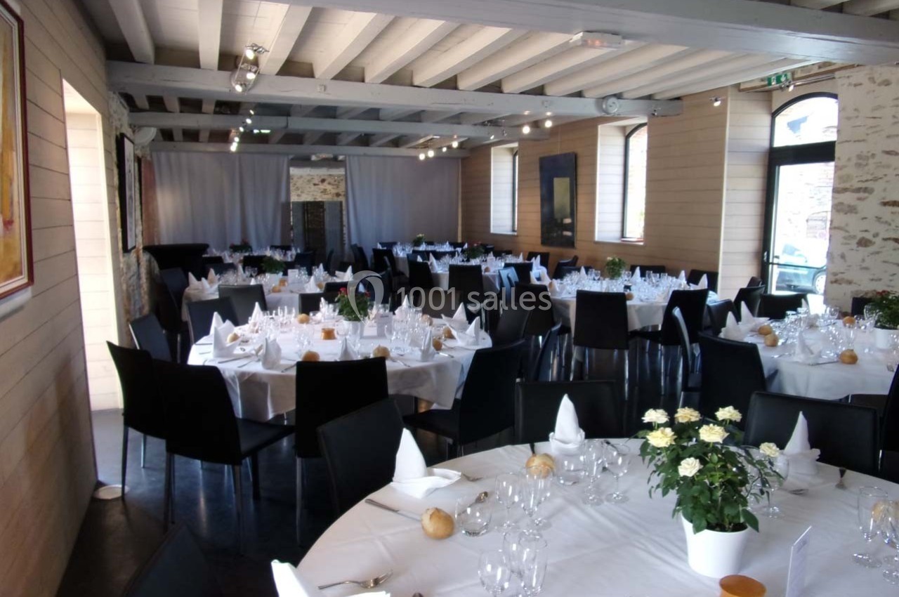 Salle de réception lumineuse avec tables rondes dressées, nappes blanches, vaisselle élégante et décoration florale.
