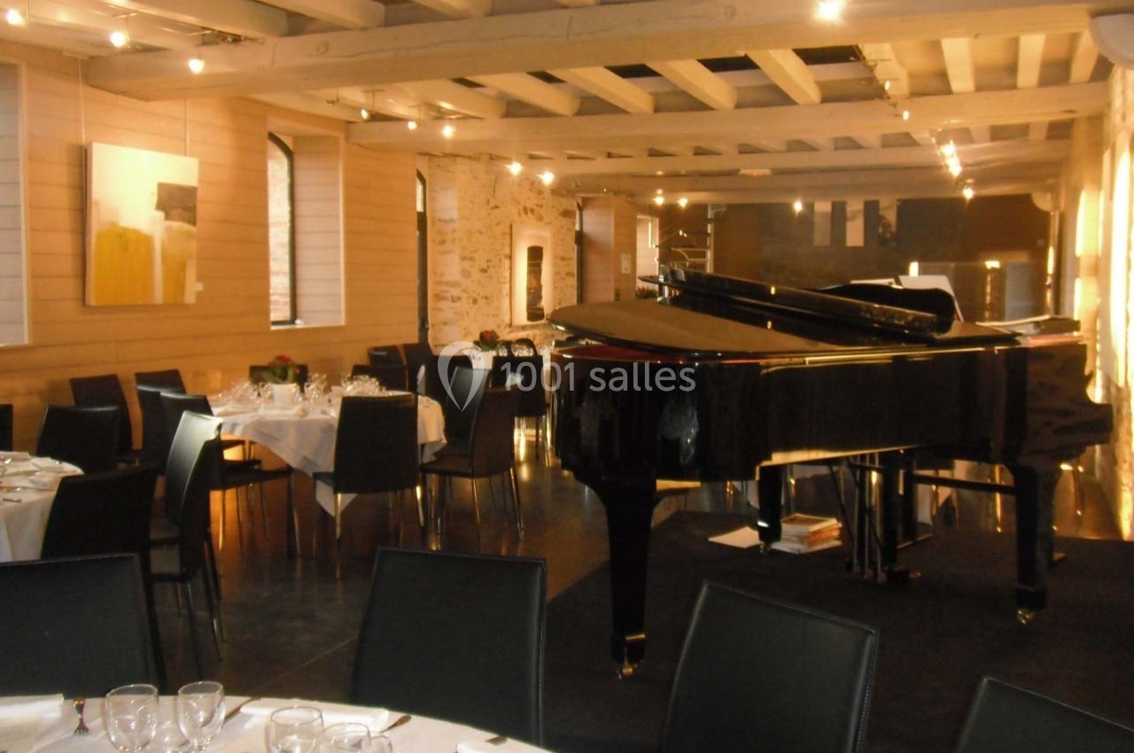 Salle de réception élégante avec un piano à queue noir, tables dressées et murs en pierre apparente.