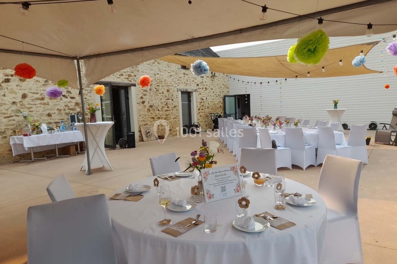 Tables décorées pour un événement en plein air sous des tonnelles, avec guirlandes et fleurs colorées.