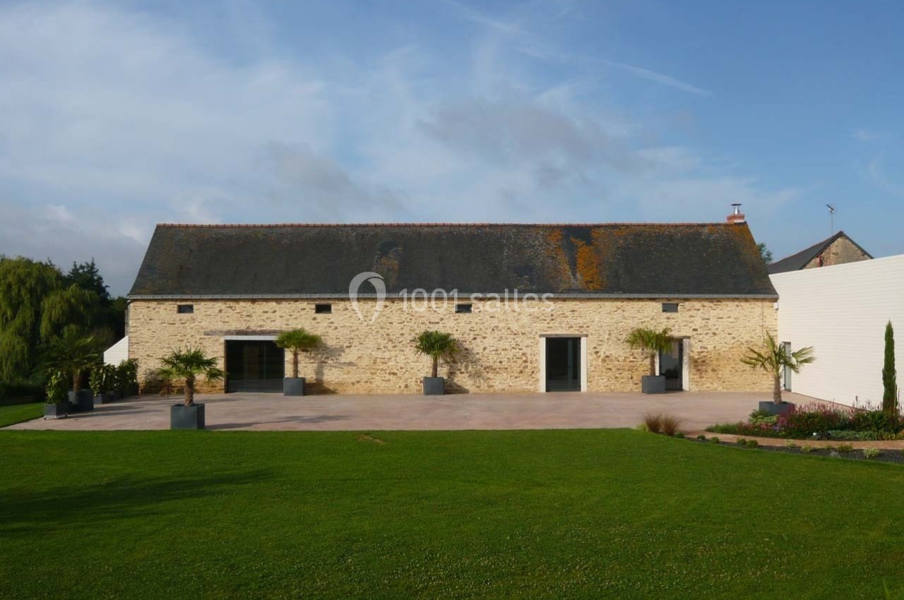 Façade d'une grange en pierre rénovée avec toit en ardoise, entourée d'une cour pavée et d'une pelouse entretenue.