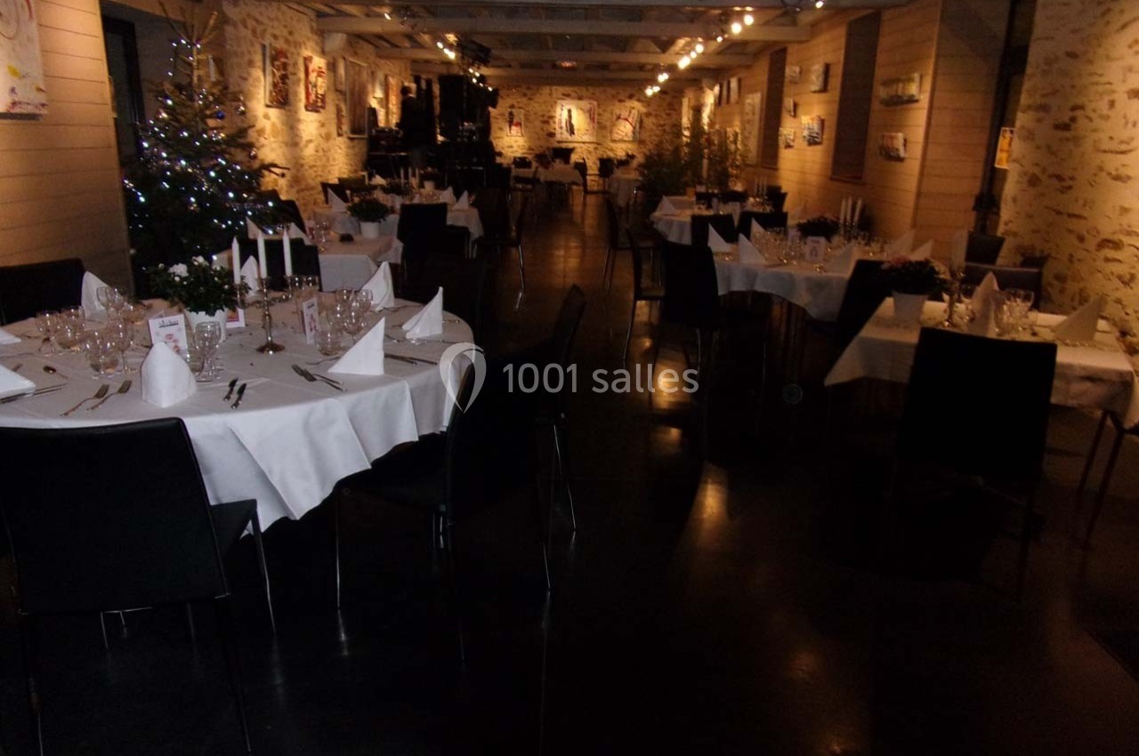 Salle de réception décorée avec des tables rondes dressées, éclairage tamisé et sapins de Noël en arrière-plan.