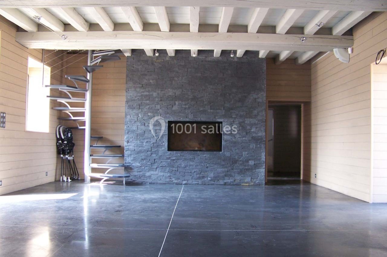 Intérieur moderne avec mur en pierre, cheminée encastrée, escalier métallique en colimaçon et sol en béton poli.