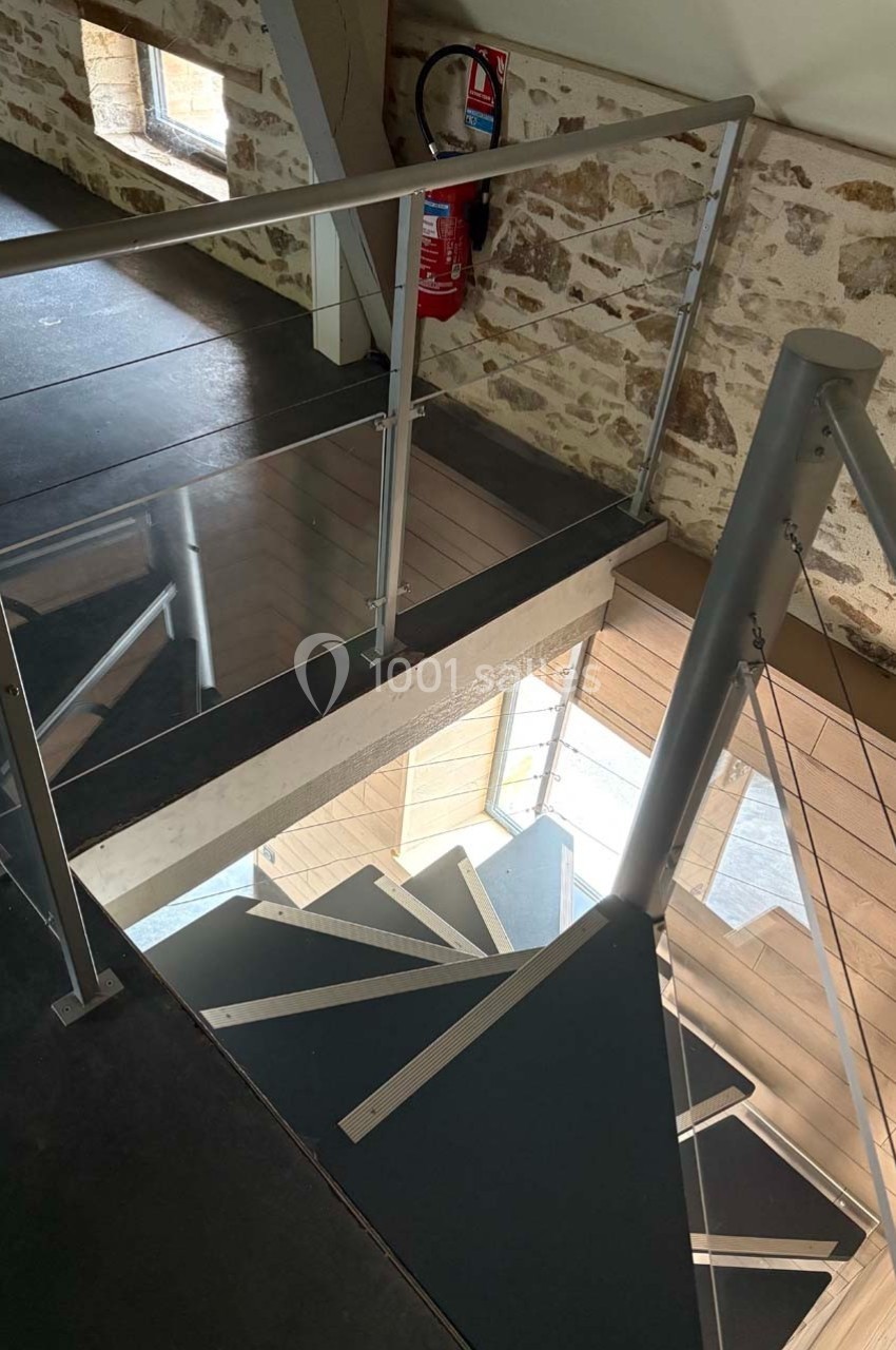 Escalier en colimaçon moderne avec garde-corps en verre, situé dans un intérieur aux murs en pierre apparente.