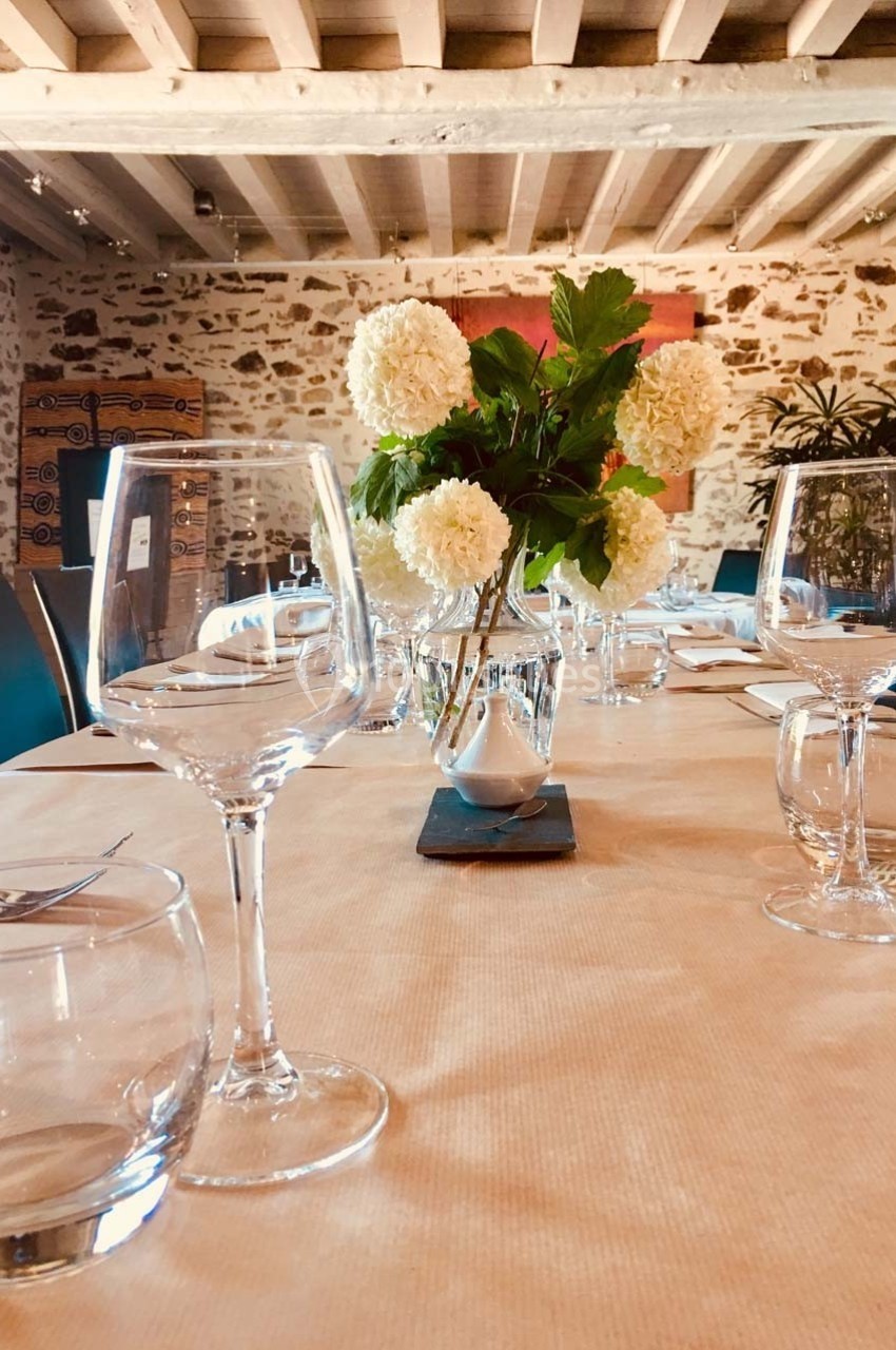 Table dressée avec des verres, un vase de fleurs blanches et un décor intérieur en pierre et poutres apparentes.