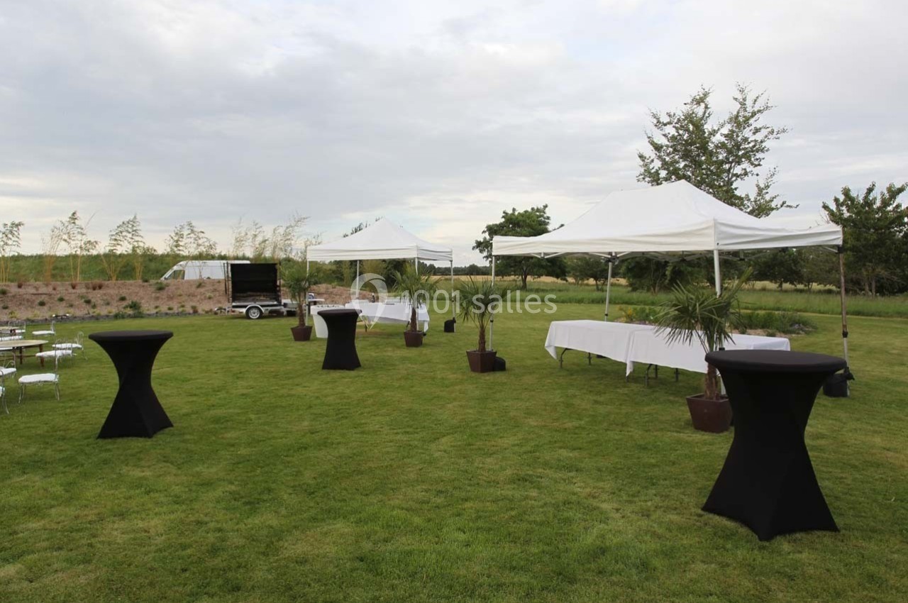 Tentes blanches et tables hautes noires installées sur une pelouse pour un événement en plein air.