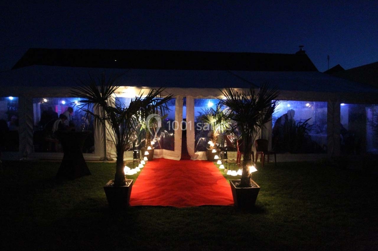 Tente éclairée de nuit avec tapis rouge et palmiers en pot, créant une ambiance festive.