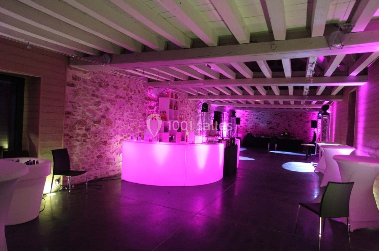 Salle de réception avec murs en pierre, éclairage rose, bar lumineux et mobilier moderne.