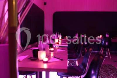 Scène de DJ éclairée par des lumières colorées, entourée de rideaux rouges et de haut-parleurs dans une salle.