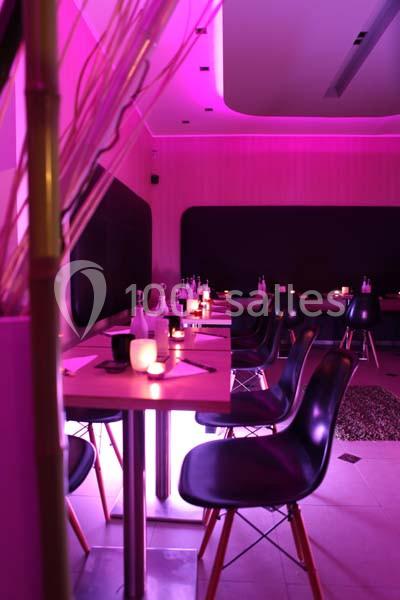 Salle de restaurant moderne avec éclairage rose, tables dressées et chaises noires.
