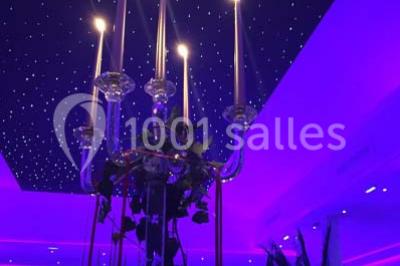 Scène de DJ éclairée par des lumières colorées, entourée de rideaux rouges et de haut-parleurs dans une salle.