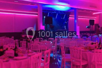 Scène de DJ éclairée par des lumières colorées, entourée de rideaux rouges et de haut-parleurs dans une salle.