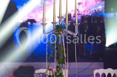 Scène de DJ éclairée par des lumières colorées, entourée de rideaux rouges et de haut-parleurs dans une salle.