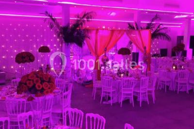 Scène de DJ éclairée par des lumières colorées, entourée de rideaux rouges et de haut-parleurs dans une salle.