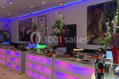 Scène de DJ éclairée par des lumières colorées, entourée de rideaux rouges et de haut-parleurs dans une salle.