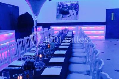 Scène de DJ éclairée par des lumières colorées, entourée de rideaux rouges et de haut-parleurs dans une salle.