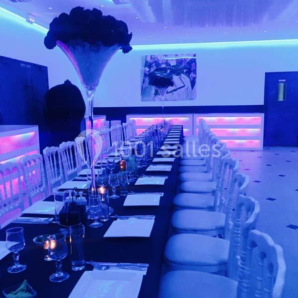 Salle de réception avec une longue table dressée, éclairage tamisé et décorations lumineuses colorées.