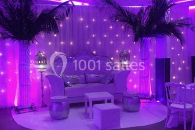 Scène de DJ éclairée par des lumières colorées, entourée de rideaux rouges et de haut-parleurs dans une salle.