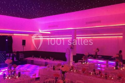 Scène de DJ éclairée par des lumières colorées, entourée de rideaux rouges et de haut-parleurs dans une salle.