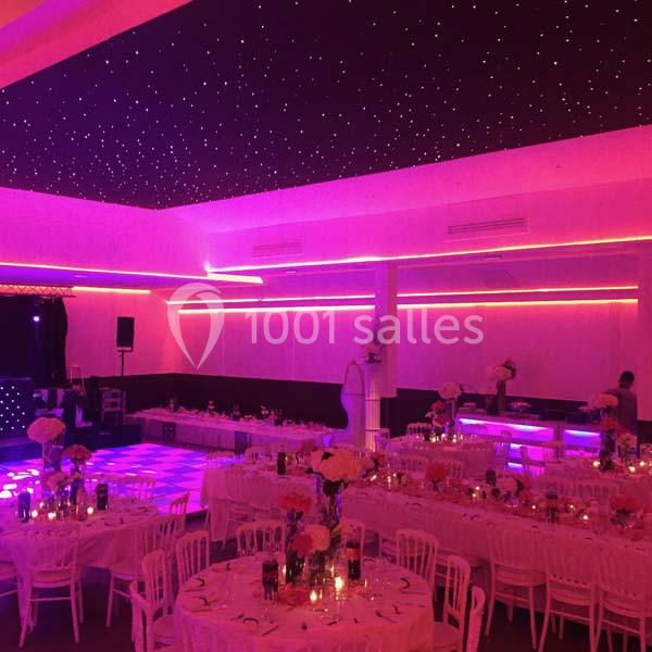 Salle de réception décorée avec des tables dressées, éclairage rose et plafond étoilé lumineux.