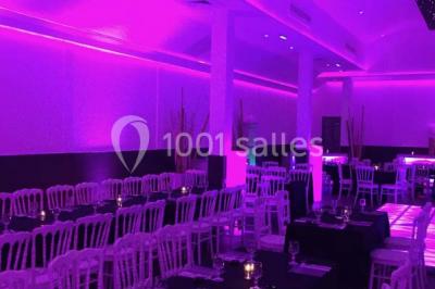 Scène de DJ éclairée par des lumières colorées, entourée de rideaux rouges et de haut-parleurs dans une salle.