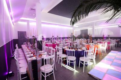 Scène de DJ éclairée par des lumières colorées, entourée de rideaux rouges et de haut-parleurs dans une salle.