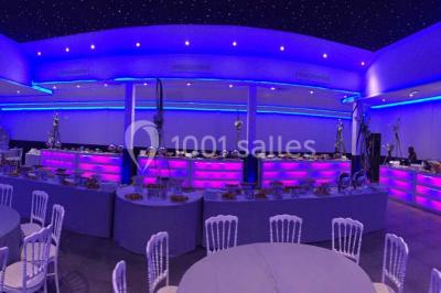 Scène de DJ éclairée par des lumières colorées, entourée de rideaux rouges et de haut-parleurs dans une salle.