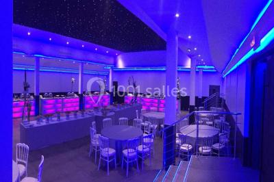 Scène de DJ éclairée par des lumières colorées, entourée de rideaux rouges et de haut-parleurs dans une salle.