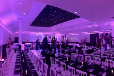 Scène de DJ éclairée par des lumières colorées, entourée de rideaux rouges et de haut-parleurs dans une salle.