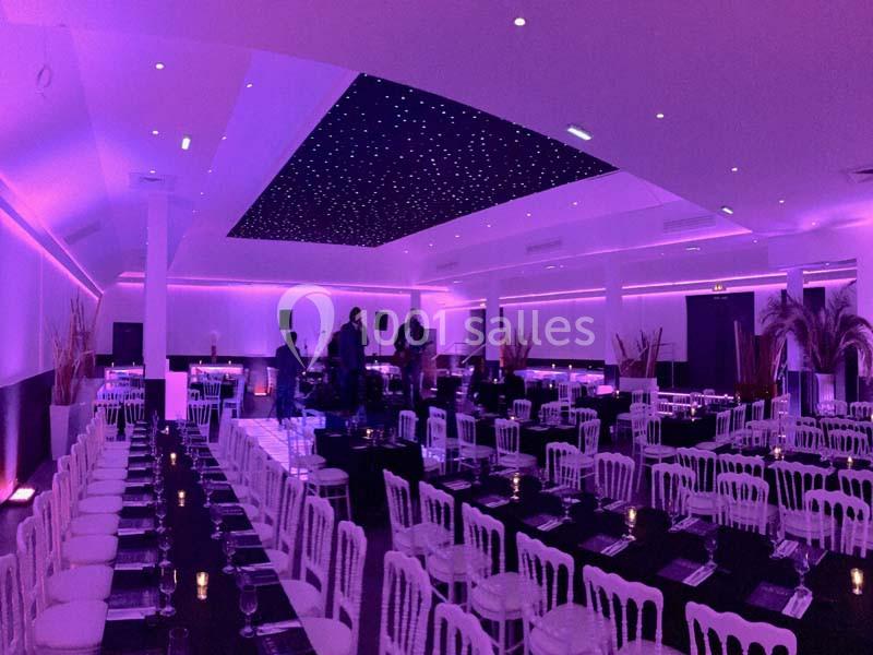Salle de réception décorée avec des tables dressées, éclairage violet et plafond étoilé lumineux.