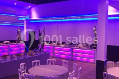 Scène de DJ éclairée par des lumières colorées, entourée de rideaux rouges et de haut-parleurs dans une salle.