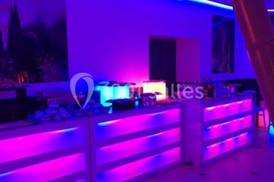 Scène de DJ éclairée par des lumières colorées, entourée de rideaux rouges et de haut-parleurs dans une salle.