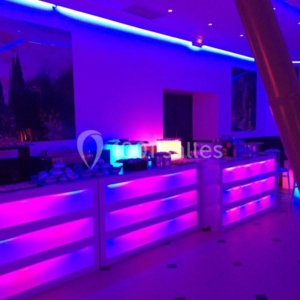 Comptoirs lumineux violets et bleus dans une salle de réception, avec des boissons et des plats disposés.