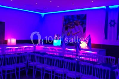 Scène de DJ éclairée par des lumières colorées, entourée de rideaux rouges et de haut-parleurs dans une salle.